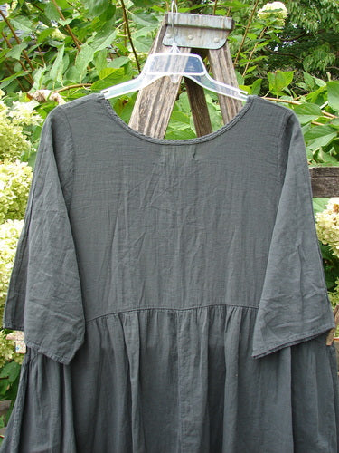 Barclay NWT Textured Terrarium Dress Contour Floral Ironworks Size 1, featuring elbow-length sleeves and a gathered skirt, hangs on a clear hanger. Displayed outdoors, showcasing its unique floral theme and textured organic cotton.