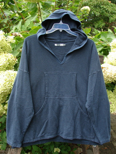 Barclay Cotton Hemp Hip To Be Square Hoodie Rear Botanicals Black OSFA, featuring a V-notch neckline, kangaroo pocket, and roomy hood, displayed outdoors against leafy shrubs and hydrangeas.