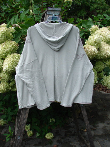 Barclay NWT Fleece Modal Hip To Be Square Hoodie Contour Floral Cloud OSFA, draped on a wooden stand, featuring a loose fit with a hood and kangaroo pocket against a garden backdrop.