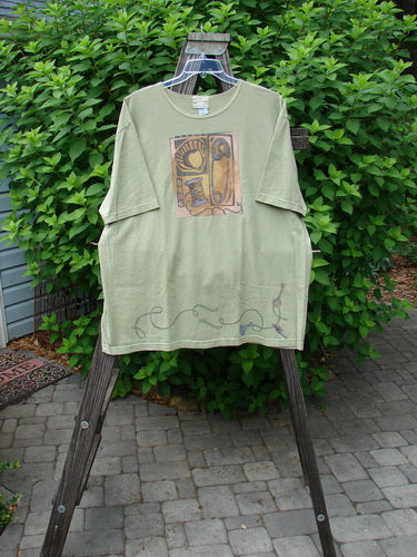 2001 NWT Short Sleeved Tee Junk Drawer Kelp Size 2 displayed on a wooden hanger, showcasing its drop shoulders, wide short sleeves, and detailed junk drawer theme paint.