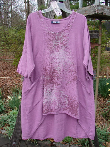 Barclay NWT Linen Poset Tunic Dress Clover Field Orchid Size 0 on a wooden pole, showcasing a flowy figure-eight shape with exterior drop front pockets and curvy panels.