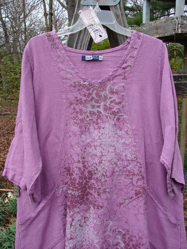 Barclay NWT Linen Poset Tunic Dress Clover Field Orchid Size 0 displayed on a hanger, showcasing its flowy figure-eight shape, oval neckline, and exterior drop front pockets.