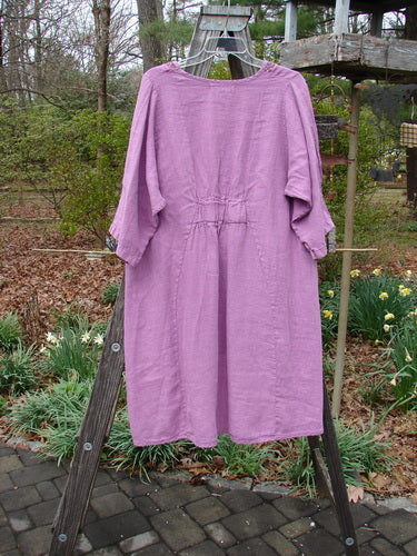 Barclay NWT Linen Poset Tunic Dress Clover Field Orchid Size 0, displayed on a wooden rack, featuring an oval neckline, flowy figure-eight shape, and exterior drop front pockets.