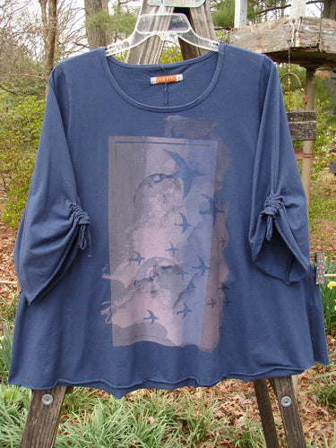 Barclay Draw Sleeve Cafe Tunic Moon Gull Denim Size 1, featuring bird artwork, rounded neckline, A-line shape, long drawstring sleeves, and rolled edges, displayed against a leafy outdoor backdrop.