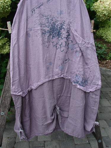 Barclay NWT Linen Explorer Jumper Tiny Botanical Sea Fog Size 0, featuring a lavender linen design with a large front pocket, floral script, and drawstring detail, draped on a wooden ladder with greenery backdrop.