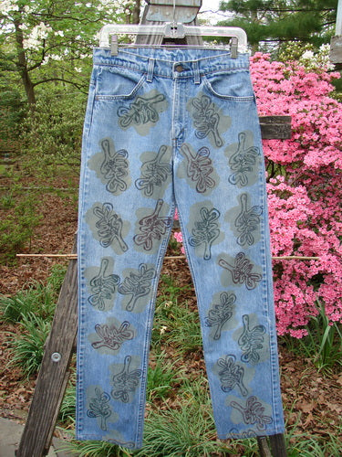 1995 Levi Strauss & Co Denim Blue Jean Leaves Stone Wash Size 1, featuring hand-decorated leaf motifs in earth tones, light-wash, with signature Blue Fish Patch, hangs outdoors on a wooden frame.