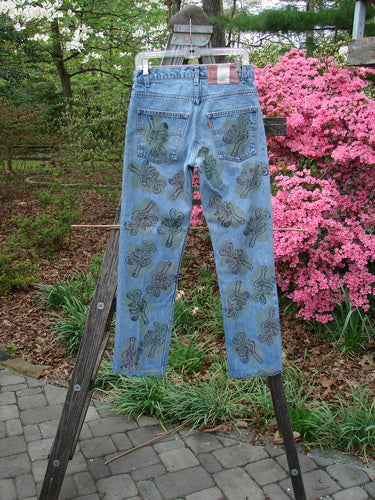 1995 Levi Strauss & Co Denim Blue Jean Leaves Stone Wash Size 1 hangs on a wooden hanger over a stepladder, showcasing its intricate leaf motif design in an outdoor garden setting.