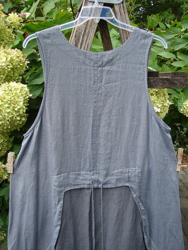 Barclay NWT Linen Explorer Jumper Trailing Botanicals Blue River Mist Size 0 hanging on a clear hanger, showcasing its sleeveless design, scoop neckline, and gathered back, set against garden foliage and wooden trellis.