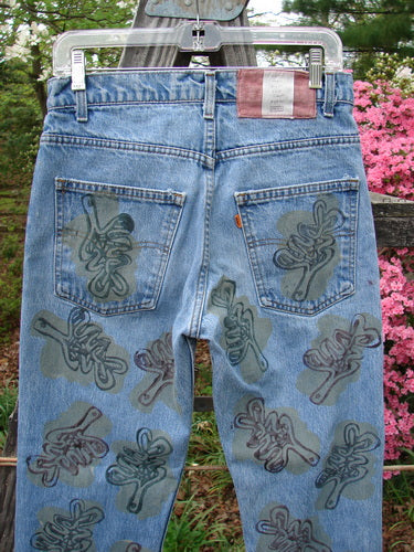 1995 Levi Strauss & Co Denim Blue Jean Leaves Stone Wash Size 1, featuring all-over leaf patterns and the iconic orange Levis tag, hangs outdoors, showcasing its vintage appeal and unique design elements.