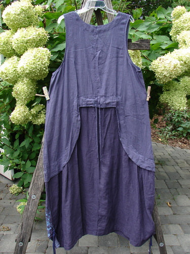 Barclay NWT Linen Explorer Jumper in Botanical Blossom Purple River Mist, displayed on a hanger against a rustic ladder. Features a scoop neckline, generous pocket, and artistic floral accents, embodying BlueFishFinder's creative freedom ethos.