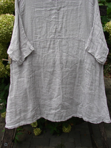 A loose-fitting Barclay NWT Linen Zen Pocket Tunic, draped over a wooden stand, features a smock style with three-quarter sleeves, dual pockets, and a varying hemline, ideal for creative expression.