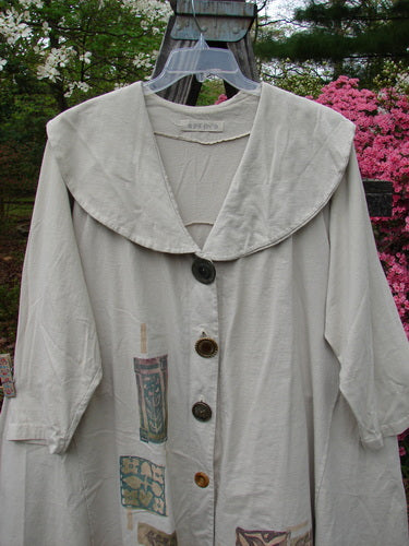 1994 Wanderer's Jacket Mindful Mosaic Mist Altered Size 1: A vintage white coat with a wide shawl collar, button details, sectional side inserts, and altered shoulders, displayed on a hanger.
