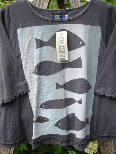 Barclay NWT Three Quarter Sleeved Crop Cafe Tee Many Fish Black Sand Size 0 features a pale-blue/gray panel with black fish silhouettes, showcasing a rolled neckline and curly edgings on a wooden rack.
