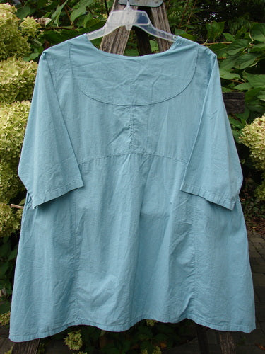 Barclay NWT Batiste Cross Over Urchin Pocket Tunic Tiny Tulip Turquoise Size 0, displayed on a clear hanger, features unique sectional panels and a cross-over neckline, embodying Bluefishfinder.com's vintage style.