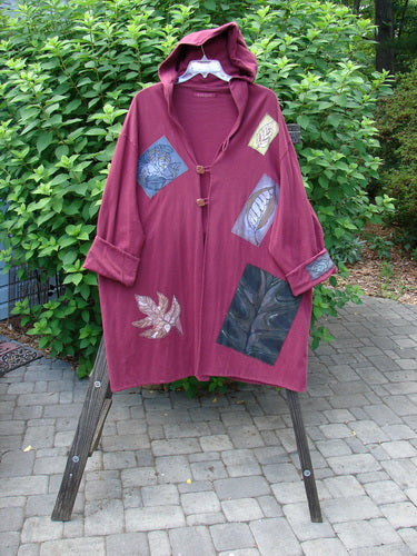 1998 Patched Autumn Coat Fall Leaf Madder OSFA displayed on a stand, featuring a cozy hood, three ceramic buttons, oversized top closure, triple-looped closures, and colorful fall-themed patches. Double-layered cotton.