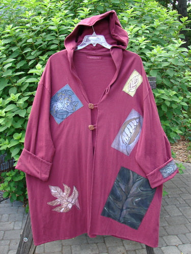 1998 Patched Autumn Coat Fall Leaf Madder OSFA: A long red hooded coat with ceramic buttons, oversized closure, foldable cuffs, drop shoulders, and large painted patches of leaves and branches.