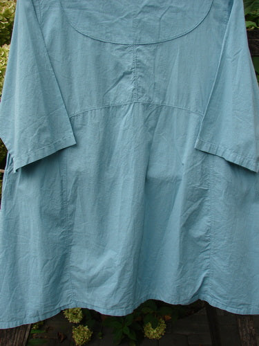 Barclay NWT Batiste Cross Over Urchin Pocket Tunic Tiny Tulip Turquoise Size 0: A loose-fitting, light-blue tunic with a rounded yoke, flared body, and two exterior pockets, hanging outdoors.
