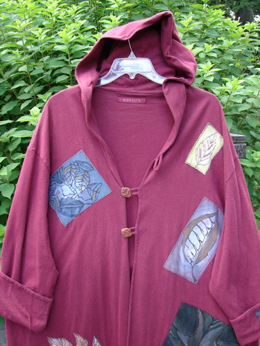 1998 Patched Autumn Coat Fall Leaf Madder OSFA featuring a cozy double-layered hood, foldable patched cuffs, triple looped closures, and vibrant fall-themed patches, including oversized leaves and branches.