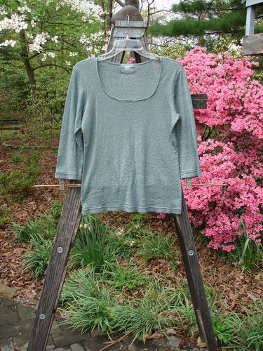 2000 Litmus Squareneck Top Unpainted Puddle Size 1 on a wooden rack, showcasing its wider rounded neckline, neatly stitched accents, and slightly flared hips, highlighting its elegant drape and light shimmer.