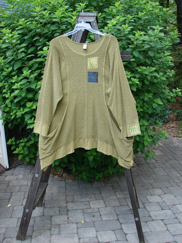 Barclay Patched Crepe Perennial Tunic Top Woods Olive Size 2 displayed on a rack, showcasing its unique textured cotton crepe fabric, two front drop wrap side pockets, and a curved empire waist seam.