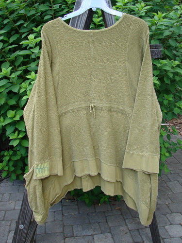 Barclay Patched Crepe Perennial Tunic Top Woods Olive Size 2 displayed on a rack, highlighting its textured cotton crepe fabric and unique design features including front pockets, curved waist seam, and varied hemline.