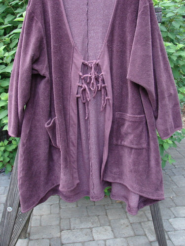 Barclay Chenille Rippie Tie Front Robe Jacket Unpainted Murple Size 2 displayed on a wooden rack, showcasing its double drop front pockets, varying hemline, and deep V-shaped neckline.