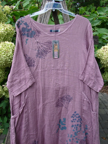 Barclay NWT Linen Wave Pocket Dress in Dried Floral Tulsi Rose, featuring ¾-length pinched sleeves, abstract botanical motifs, a rounded neckline, front drop pockets, and varying hemline, hanging outdoors.