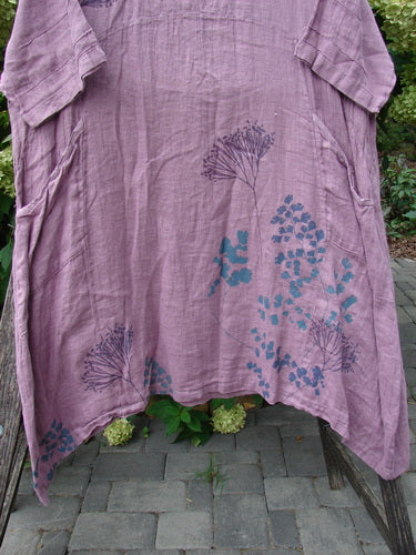 Barclay NWT Linen Wave Pocket Dress Dried Floral Tulsi Rose Size 0 with botanical prints, rounded neckline, seamless bodice, front pockets, and varying hemline, draped over a wooden chair.