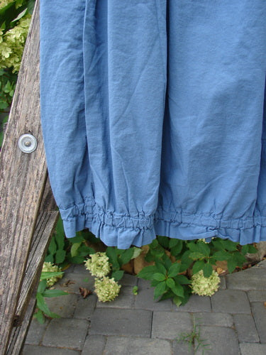 Barclay NWT Batiste Airy Lawn Skirt Unpainted Echo Blue Size 0: A blue, ankle-length skirt with a gathered hem, displayed outdoors against a stone path and leafy plants, highlighting its airy, lightweight cotton fabric.