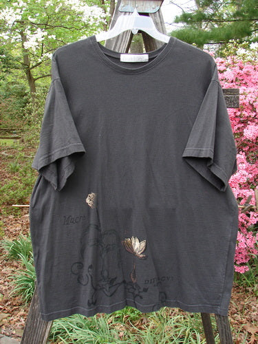 1998 Botanicals Short Sleeved Tee Macro Raven Size 2 hanging on a wooden pole, showcasing a flower design and boxy shape from Blue Fish's vintage Spring Collection.