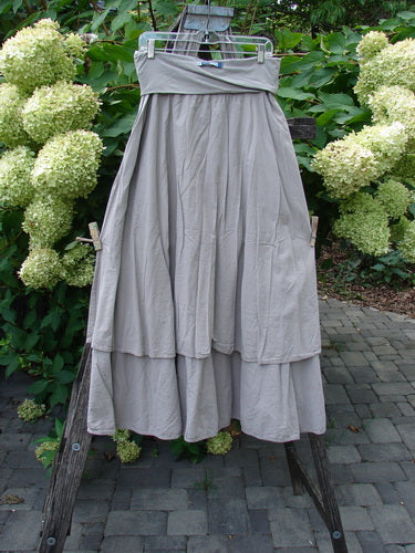 Barclay NWT Batiste Fold Over Stardust Tier Skirt Moon Rock Sand Size 0 hangs gracefully on a hanger, highlighting its two-tiered, flowing A-line design and forgiving waistline.