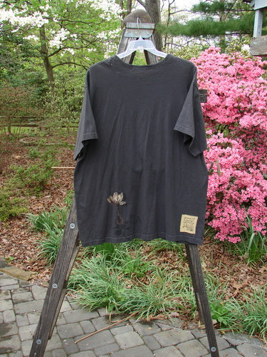 1998 Botanicals Short Sleeved Tee Macro Raven Size 2 displayed on a wooden rack, featuring a longer boxy shape, organic cotton material, and a floral design on the front.