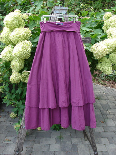 Barclay NWT Batiste Fold Over Stardust Tier Skirt in Tyrian Berry Size 0 displayed on a garden trellis, showcasing its flowing, full silhouette with a tiered design against lush green foliage.