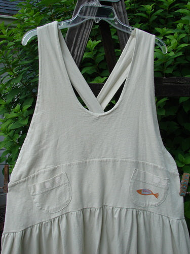 White Tadpole Jumper with sweeping hemline and adjustable straps displayed on a hanger, featuring round pockets and blue fish patch. 1999 NWT Tadpole Jumper Single Orange Pike Natural OSFA.
