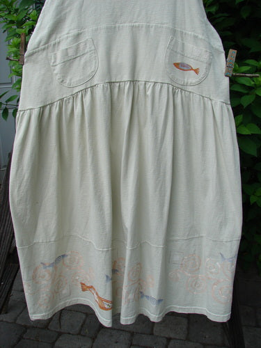 1999 NWT Tadpole Jumper in Natural with fish patterns, adjustable shoulder straps, sweeping hemline, criss-cross lower back, and round bottom pockets, featuring an orange pike and blue fish patch.