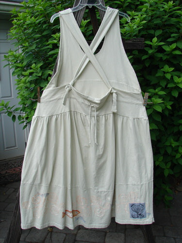 1999 NWT Tadpole Jumper Single Orange Pike Natural OSFA, hanging on a clothesline, showcases adjustable shoulder straps, a sweeping hemline, crisscross back, double-paneled waistline, and round-bottomed pockets.