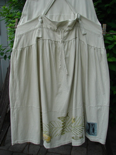 1999 NWT Tadpole Jumper Single Gold Fish Sky Natural OSFA: A long white organic cotton skirt with floral design, adjustable shoulder straps, sweeping hemline, and blue fish patch, displayed on a clothes rack.