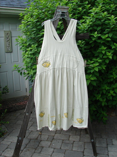 1999 NWT Tadpole Jumper Single Gold Fish Dawn Natural OSFA displayed on a wooden rack, showcasing its adjustable shoulder straps, sweeping hemline, and criss-cross lower back detailing.