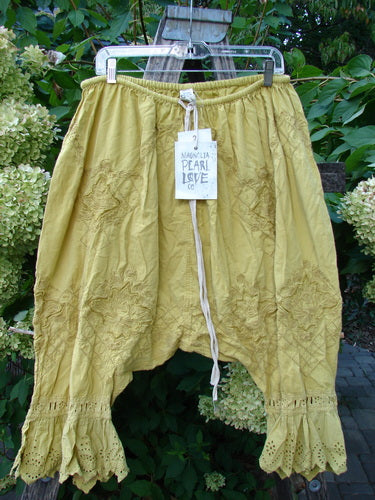Magnolia Pearl NWT Embroidered Khloe Bloomer Golden Daffodil OSFA features loose-fitting cotton bloomers with delicate eyelet-lace trim, embroidered floral patterns, and a drawstring waist, showcased outdoors against lush greenery.