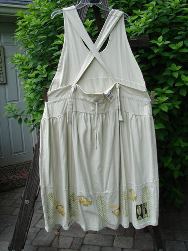 1999 NWT Tadpole Jumper Single Gold Fish Dawn Natural OSFA, featuring adjustable shoulder straps and a sweeping hemline, hanging on a clothesline outdoors, surrounded by green leaves.