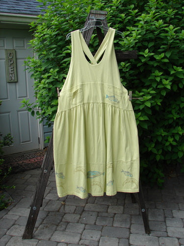 A yellow dress with a fish pattern, featuring adjustable shoulder straps, a sweeping hemline, and a criss-cross lower back. It has a yoked and empire waistline, round bottomed pockets, and a bass and moon theme paint. Made from organic cotton, this Tadpole Jumper is from the 2000 Summer Collection. Bust: 40 (open), waist: 50, hips: 60, length: 46-52 inches.