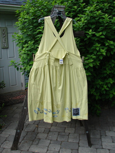 A yellow dress with adjustable shoulder straps, a sweeping hemline, and a criss-cross lower back. Features a double paneled waistline, round bottomed pockets, and a striped hem with a school theme. Made from organic cotton. 1999 NWT Tadpole Jumper Single Stripe Pike School Citron OSFA.