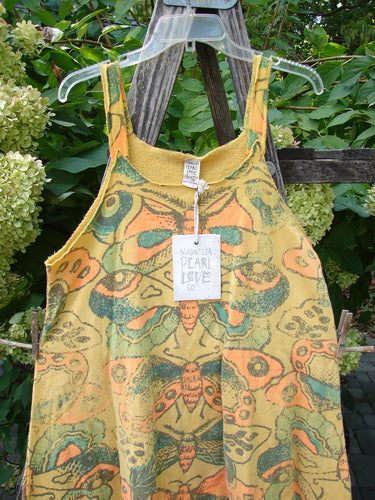 Magnolia Pearl NWT Cotton Fleece Lepidoptera Lana Tank Dress Butterfly Sunnies OSFA hangs on a clear hanger, showcasing its mustard-yellow fabric adorned with moth and butterfly patterns against a rustic backdrop.