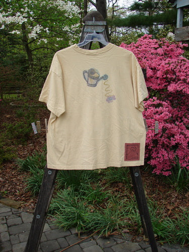 1995 Short Sleeved Tee Garden Water Glint Size 1 displayed on a rack, featuring a thick ribbed neckline, drop shoulders, and a detailed garden water theme paint, showcasing its boxy shape.