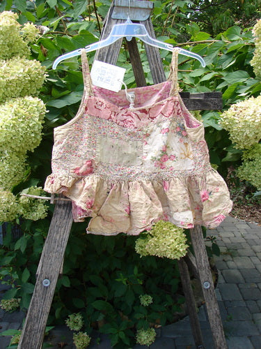 Magnolia Pearl NWT Quilted Catalina Tank Ragdoll Calico OSFA displayed on a ladder, showcasing its floral patchwork design, thin straps, ruffled hem, and distinctive quilting against a garden backdrop.