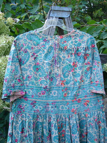 Magnolia Pearl NWT European Cotton Block Print Taigi Dress Demi OSFA features a floral-paisley print with pintucks, pleats, and ric rack accents, hanging outdoors against leafy shrubs, showcasing its sweeping hemline.