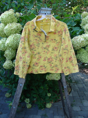 Magnolia Pearl NWT Cotton Fleece Asher Pullover Sweatshirt Vintage Rose Sunnies OSFA, featuring a pale yellow floral design, half-zip collar, and distressed accents, displayed on a wooden hanger in a garden setting.