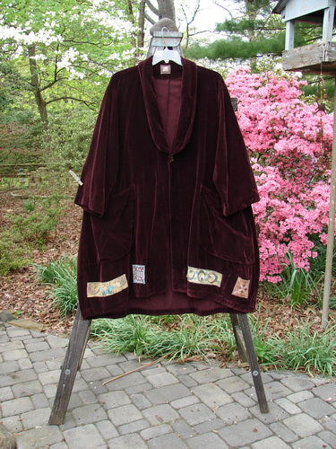 1999 Patched Velveteen Poet's Coat Holiday Deep Burgundy Size 1, displayed on a rack, showcasing oversized button closures, colorful patched hem, and two front floppy pockets with a folded collar.