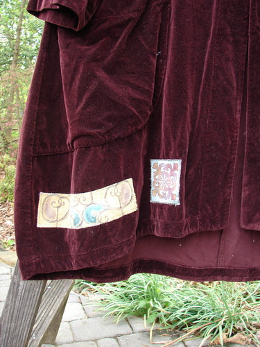 Close-up of the 1999 Patched Velveteen Poet's Coat Holiday Deep Burgundy Size 1, showcasing its oversized vintage button closures, colorful patched hem, folded collar, and front oversized floppy pockets.