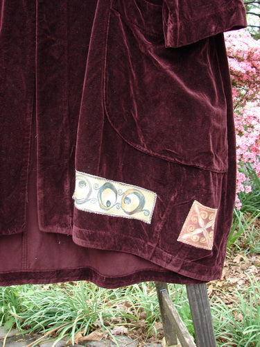 Close-up of the 1999 Patched Velveteen Poet's Coat Holiday Deep Burgundy Size 1, showcasing the smooth cotton velveteen fabric, oversized vintage button closures, and colorful patched hem.